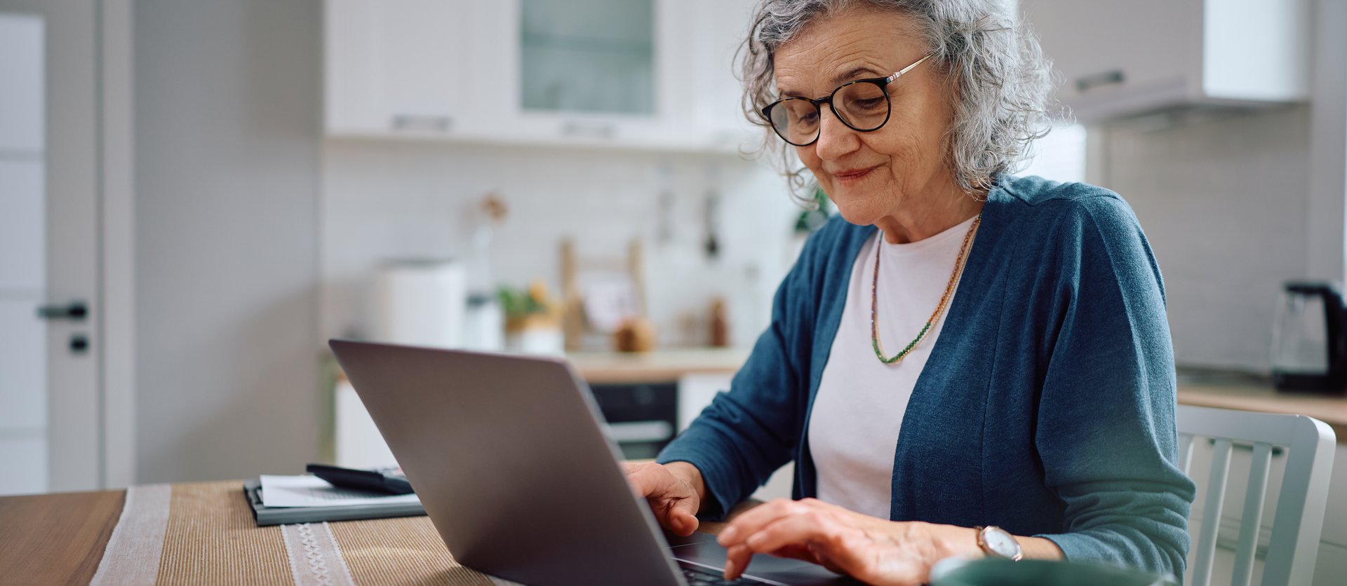 Ältere Mieterin sitzt am Küchentisch am Laptop