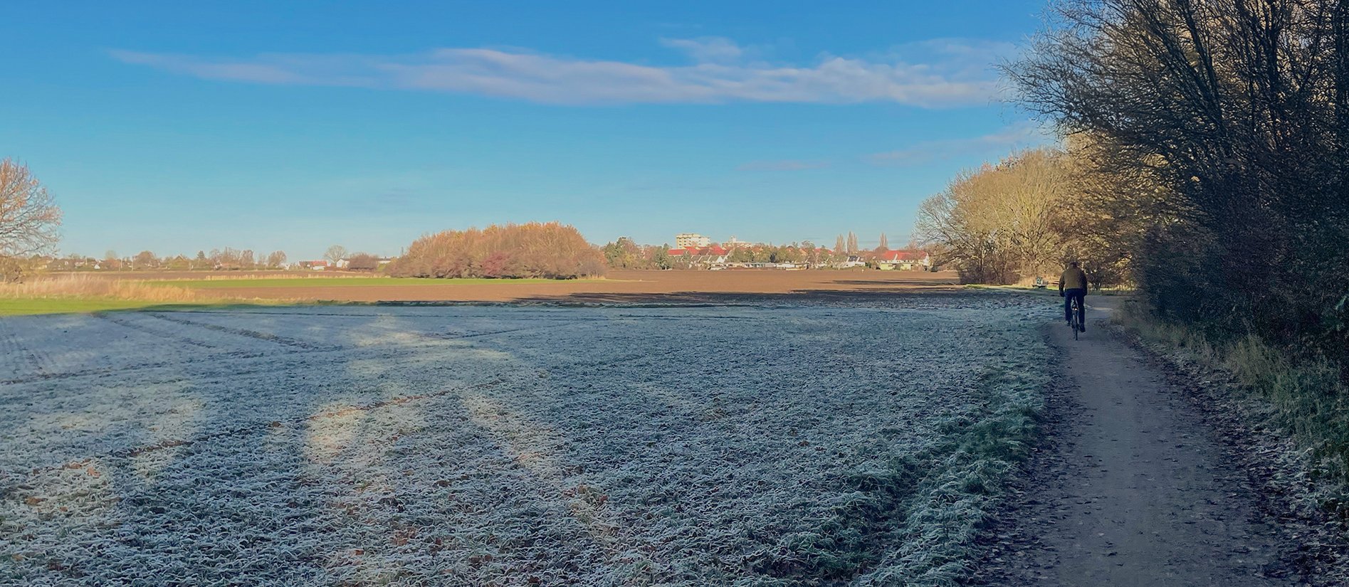 Blick über Felder und auf Radfahrer auf Fahrradweg in winterlicher Landschaft