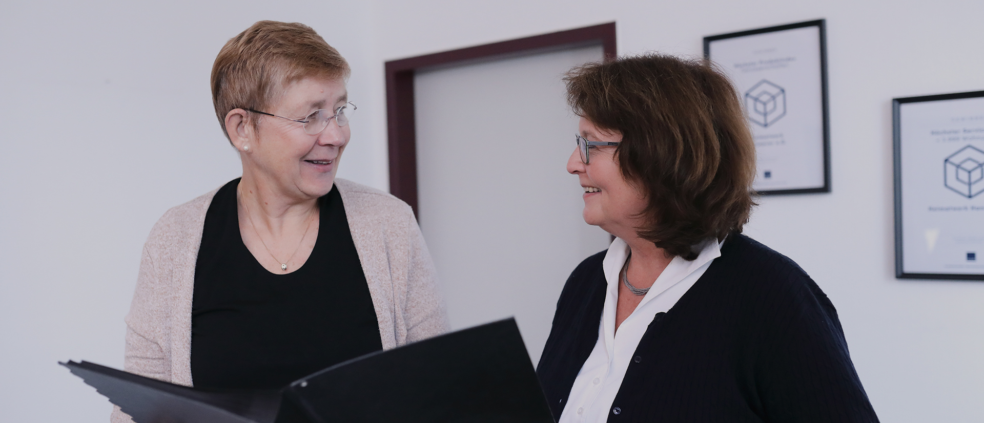 Zwei Damen mit Dokumentenmappe beim Gespräch im Büro